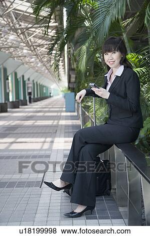 Stock Photo - Side profile of a businesswoman sitting on a railing and holding a mobile phone. Fotosearch
