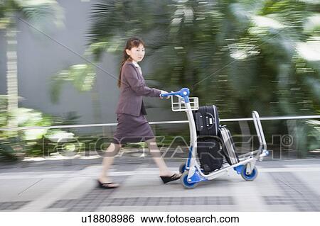Stock Photograph - Side profile of a woman pushing a luggage cart. Fotosearch
