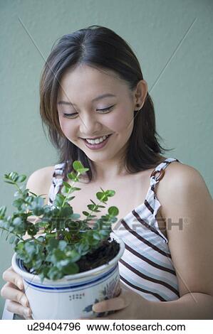 Close-up of a young woman holding a potted plant and smiling View Large Photo Image Stock Photograph - Close-up of a young woman holding a potted plant and smiling. Fotosearch
