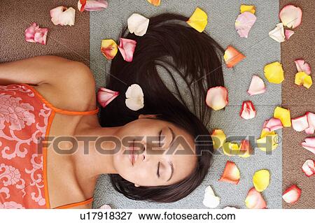 Stock Photo - High angle view of a young woman lying down with petals around her. Fotosearch
