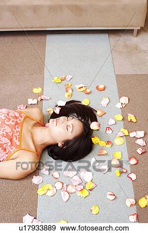 Stock Photo - High angle view of a young woman lying down on the floor with petals around her. Fotosearch