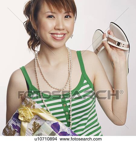 Picture - Portrait of a young woman holding a pair of slipper and smiling. Fotosearch