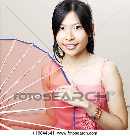 Stock Image - Portrait of a young woman holding a parasol and smiling. Fotosearch