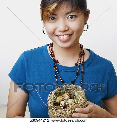 Stock Image - Portrait of a young woman holding eggs in a bird's nest and smiling. Fotosearch