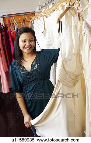 Stock Photography - Portrait of a young woman holding a dress in a clothing store. Fotosearch
