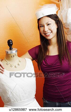 Stock Photo - Portrait of a young woman standing with her arm around a mannequin. Fotosearch