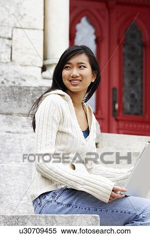 Stock Photography - Side profile of a young woman holding a laptop and smiling. Fotosearch