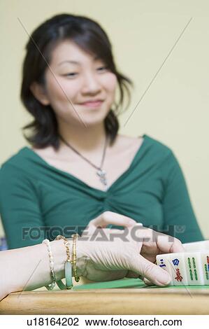 Stock Image - Close-up of a woman's hand playing with blocks and a young woman sitting in the background. Fotosearch