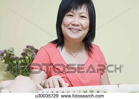 Stock Photo - Portrait of a mature woman playing mahjong and smiling. Fotosearch