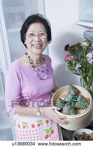 Portrait of a senior woman holding dumplings in a bamboo steamer View Large Photo Image Picture - Portrait of a senior woman holding dumplings in a bamboo steamer. Fotosearch