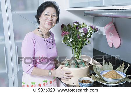 Stock Image - Portrait of a senior woman holding dumplings in a bamboo steamer. Fotosearch