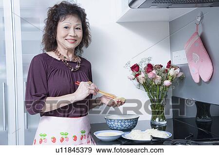 Stock Photo - Portrait of a senior woman holding chopsticks in a domestic kitchen. Fotosearch