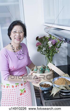 Stock Photograph - Portrait of a senior woman holding dumplings in a bamboo steamer. Fotosearch