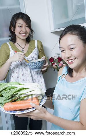 Stock Photography - Portrait of two young women preparing food in a kitchen. Fotosearch