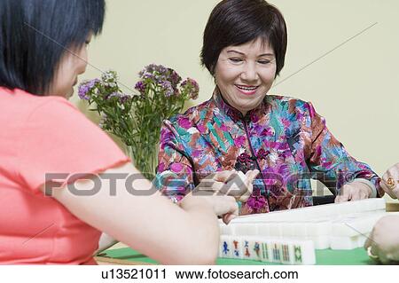 Stock Image - Senior woman and a mature woman playing mahjong. Fotosearch