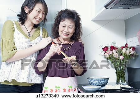 Senior woman preparing food with her granddaughter standing behind her and smiling View Large Photo Image Stock Photo - Senior woman preparing food with her granddaughter standing behind her and smiling. Fotosearch