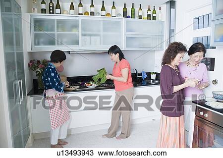 Stock Image - Three senior women and a mature woman preparing food in a domestic kitchen. Fotosearch