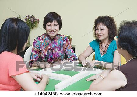 Stock Photo - Three senior women and a mature woman playing mahjong. Fotosearch