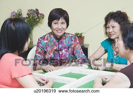 Stock Photo - Three senior women and a mature woman playing mahjong. Fotosearch