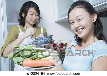 Picture - Two young women preparing food in a kitchen. Fotosearch