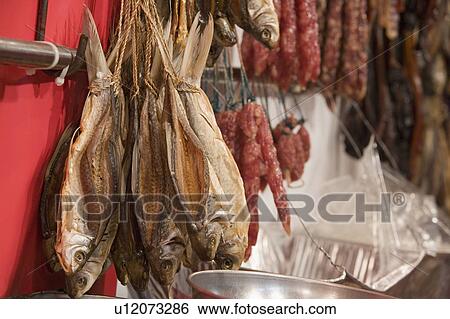 Stock Photograph - Close-up of a dried fish and sausages at a market stall. Fotosearch