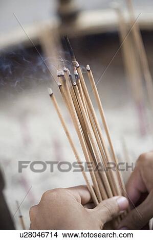 Picture - Close-up of a person's hand holding incense sticks in a temple. Fotosearch