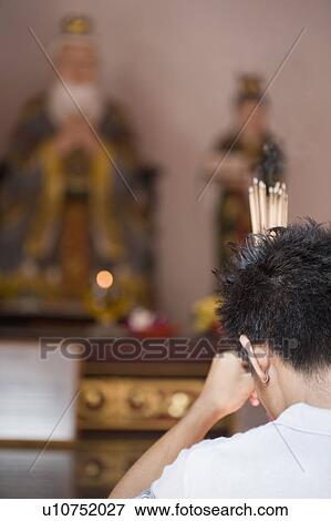 Stock Photo - Rear view of a young man praying in a temple. Fotosearch