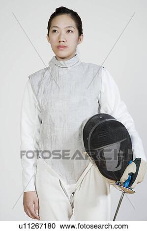 Stock Image - Close-up of a female fencer holding a fencing foil and a fencing mask. Fotosearch