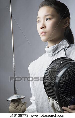 Stock Image - Close-up of a female fencer holding a sword and a fencing mask. Fotosearch