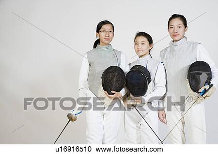 Stock Image - Portrait of three female fencers holding fencing foils and fencing masks. Fotosearch