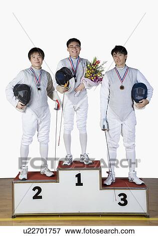 Stock Photo - Portrait of three young men in fencing costumes standing on a winner's podium. Fotosearch