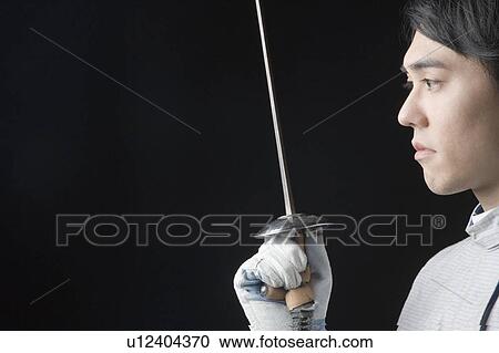 Stock Image - Side profile of a male fencer holding a fencing foil. Fotosearch
