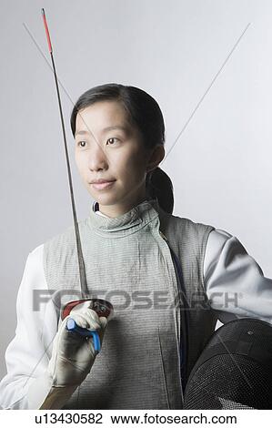 Stock Image - Close-up of a female fencer holding a sword and a fencing mask. Fotosearch