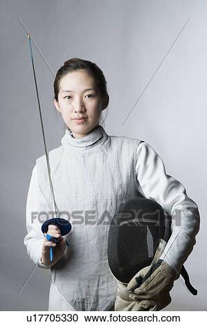 Stock Image - Portrait of a female fencer holding a sword and a fencing mask. Fotosearch