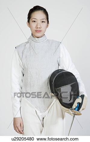 Stock Image - Portrait of a female fencer holding a fencing foil and a fencing mask. Fotosearch