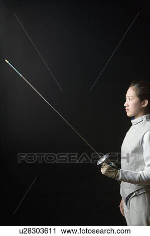 Stock Image - Side profile of a female fencer holding a fencing foil. Fotosearch