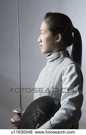 Stock Photo - Side profile of a female fencer holding a sword and a fencing mask. Fotosearch