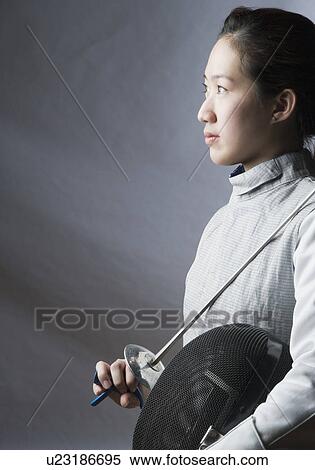 Stock Photography - Side profile of a female fencer holding a sword and a fencing mask. Fotosearch