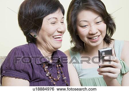 Stock Photograph - Close-up of a senior woman and her granddaughter looking at a mobile phone and smiling. Fotosearch