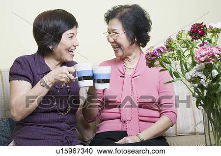 Stock Image - Close-up of two senior women toasting with cups and laughing. Fotosearch