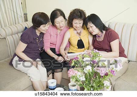 High angle view of three senior women and a mature woman sitting on a couch and looking at a photo album View Large Photo Image Picture - High angle view of three senior women and a mature woman sitting on a couch and looking at a photo album. Fotosearch