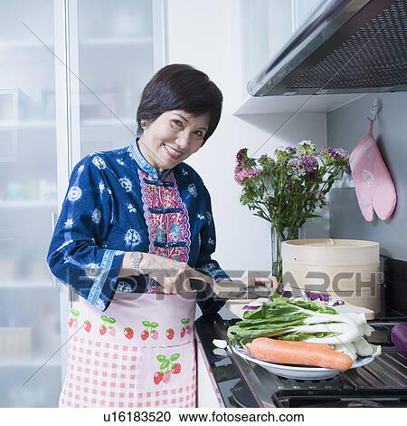 Stock Image - Portrait of a senior woman cutting vegetables and smiling. Fotosearch