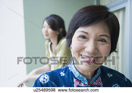 Stock Photo - Portrait of a senior woman smiling with her granddaughter standing behind her. Fotosearch