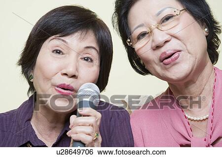Stock Photograph - Portrait of two senior women singing into a microphone. Fotosearch