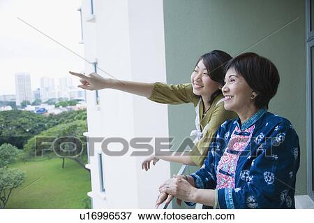 Stock Photo - Side profile of a senior woman standing in a balcony with her granddaughter. Fotosearch
