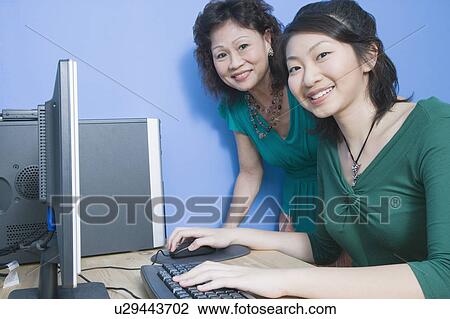 Side profile of a young woman using a computer with her mother standing beside her View Large Photo Image Stock Image - Side profile of a young woman using a computer with her mother standing beside her. Fotosearch