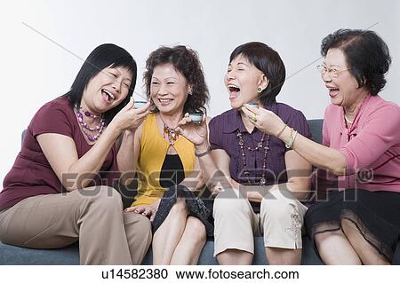 Stock Image - Three senior women and a mature woman holding tea cups and laughing. Fotosearch