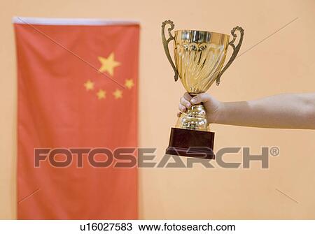 Stock Image - Close-up of a person's hand holding a golden trophy cup. Fotosearch