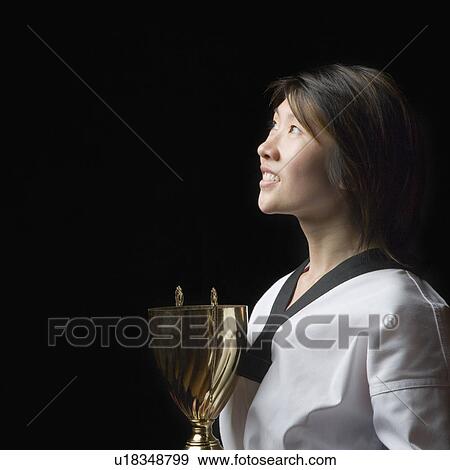 Side profile of a young woman holding a trophy View Large Photo Image Stock Photo - Side profile of a young woman holding a trophy. Fotosearch