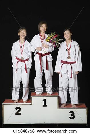 Three young women standing on a winners podium with their medals and smiling View Large Photo Image Stock Photo - Three young women standing on a winners podium with their medals and smiling. Fotosearch